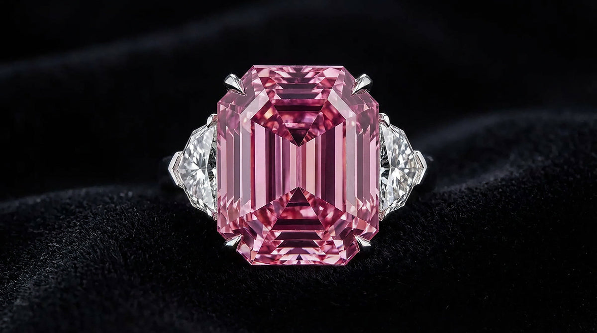 An emerald-cut pink diamond set in a white gold ring, showing the saturated color that drives value.