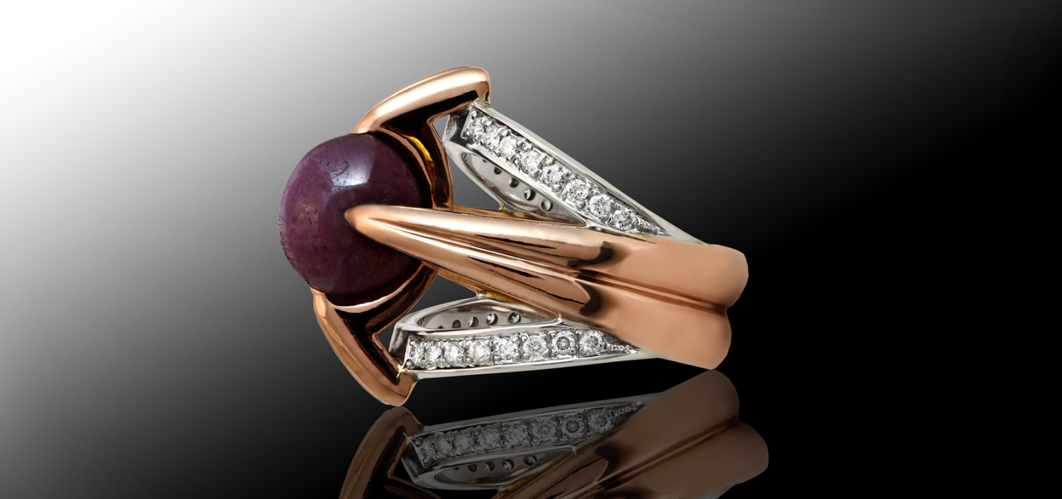 Custom-made by Garo Demirjian, a ruby star sapphire ring with 18k white and rose gold accents and diamond detailing, showcased on a reflective surface.