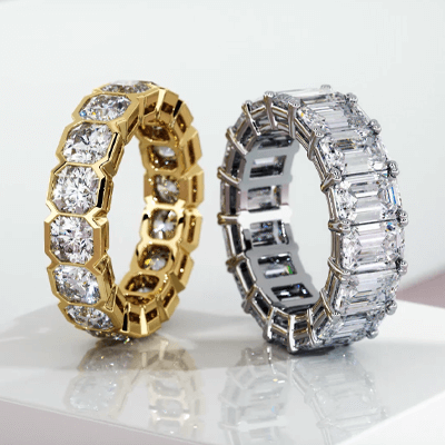 Two diamond baguette rings, one in yellow gold and one in white gold, sitting on a glossy table.