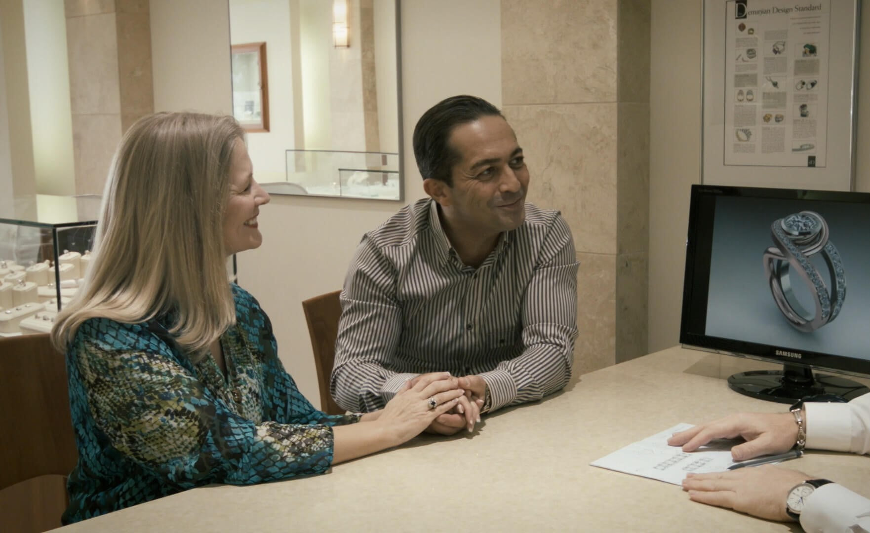 A customer and jeweler review a custom ring design on a computer during a consultation.