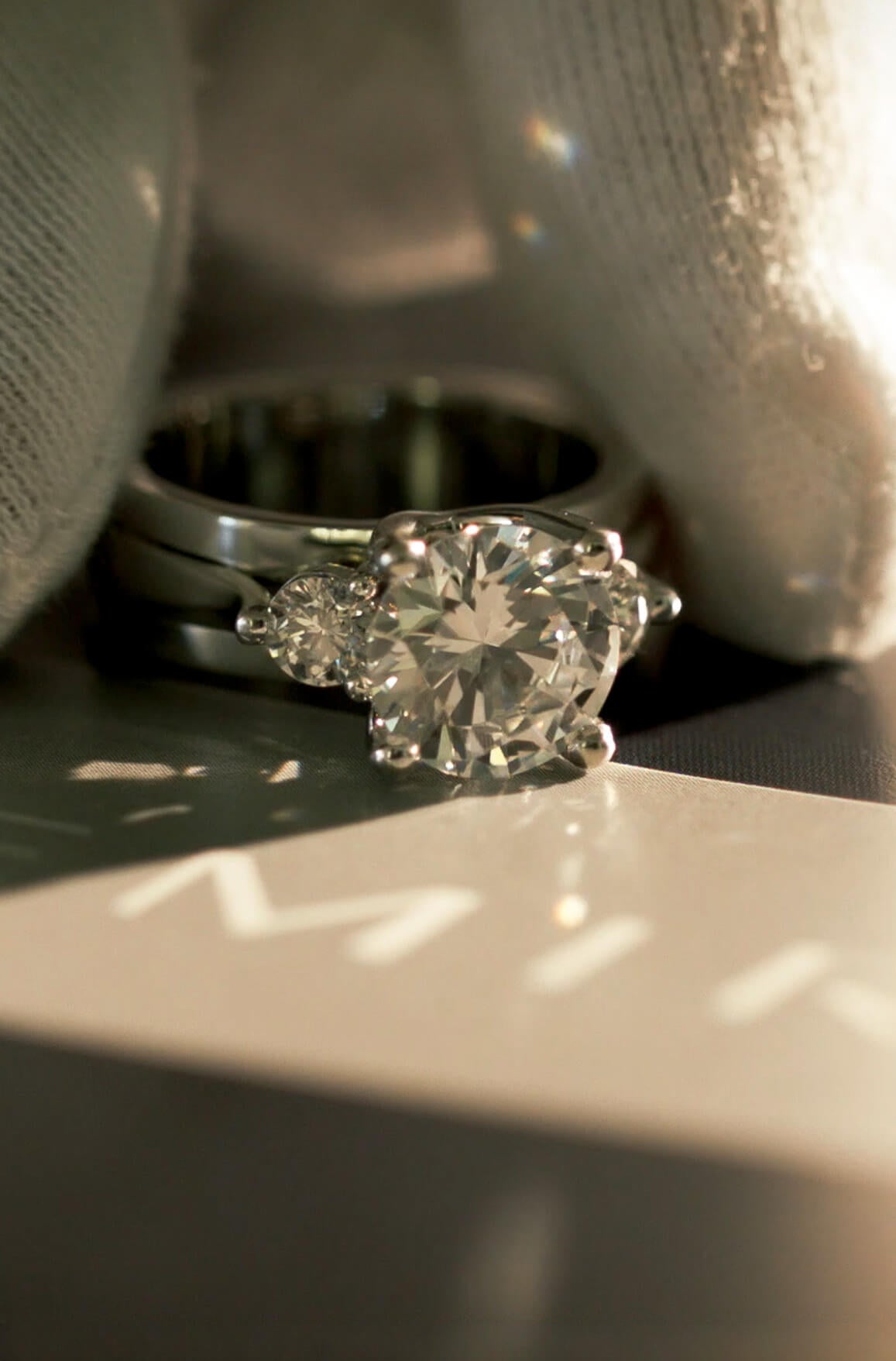 Close-up of a Demirjian custom three-stone engagement ring, showcasing a round brilliant center diamond with two side diamond stones.