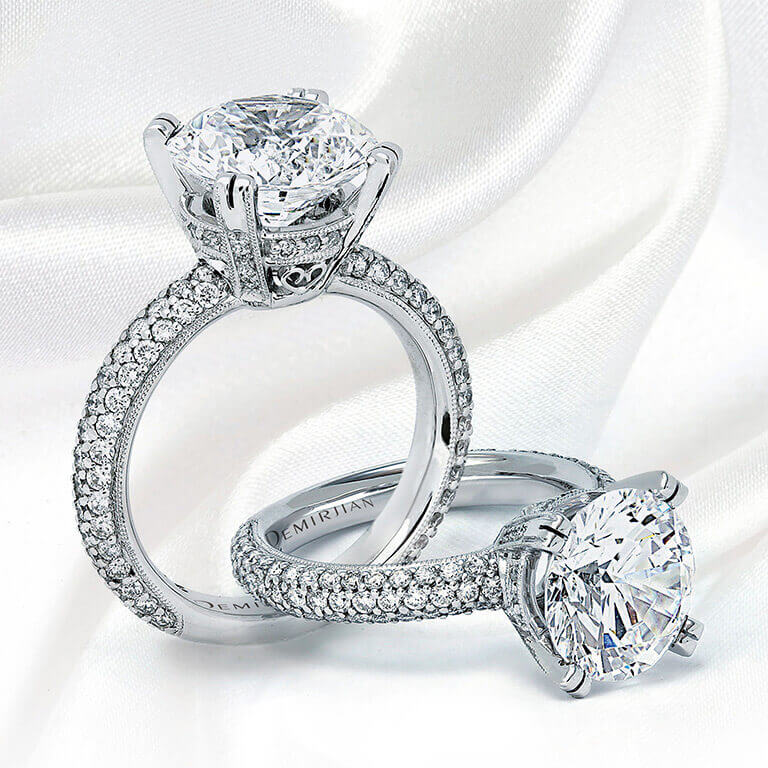 A custom pair of diamond engagement rings, prominently displaying a large central diamond, set against a white fabric backdrop.