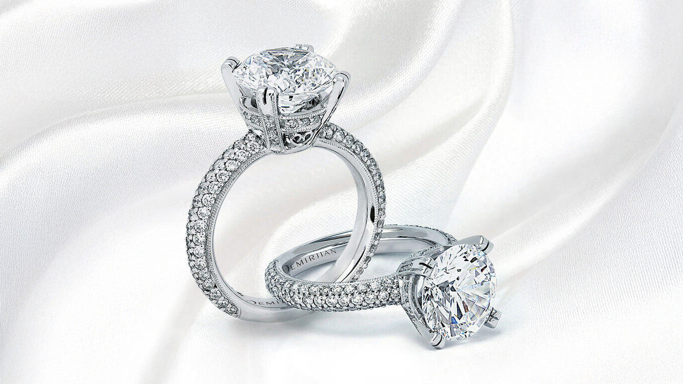 Two Demirjian custom round diamond engagement rings featuring a basket hidden halo and thick multi-row pavé diamonds around the shank.