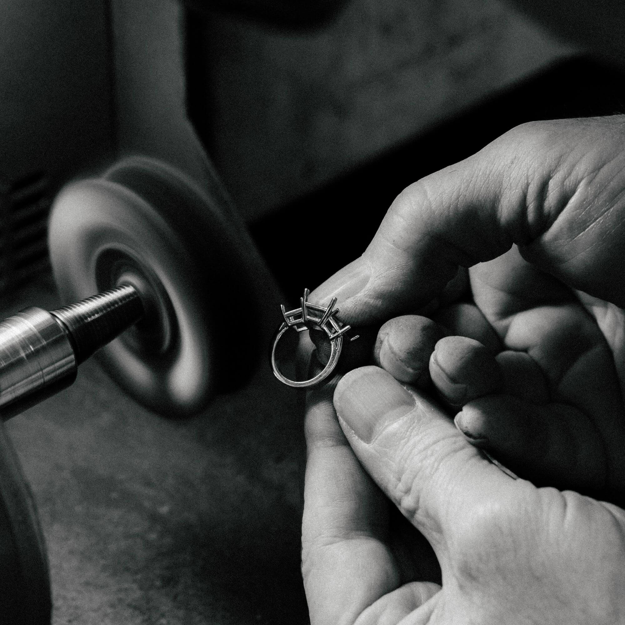 Close-up of a jeweler hand-polishing a custom three-stone diamond ring on a buffing wheel to achieve a high shine.