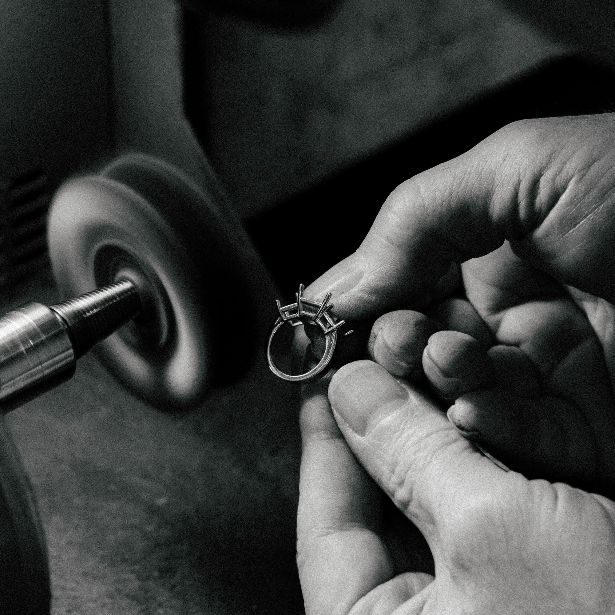 Close-up of a jeweler hand-polishing a custom three-stone diamond ring on a buffing wheel to achieve a high shine.