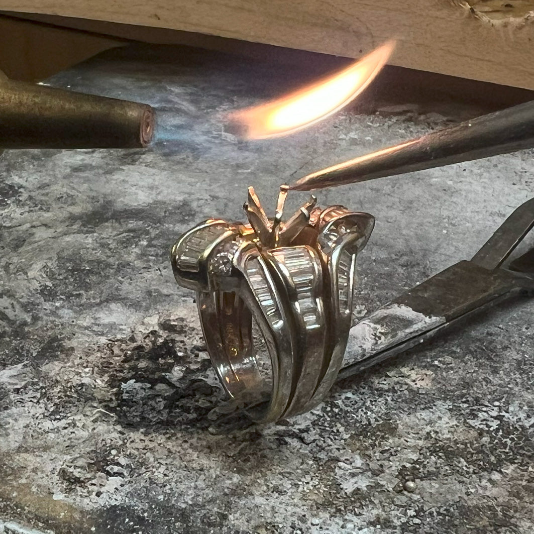 A ring with diamonds being re-tipped with a blowtorch. 
