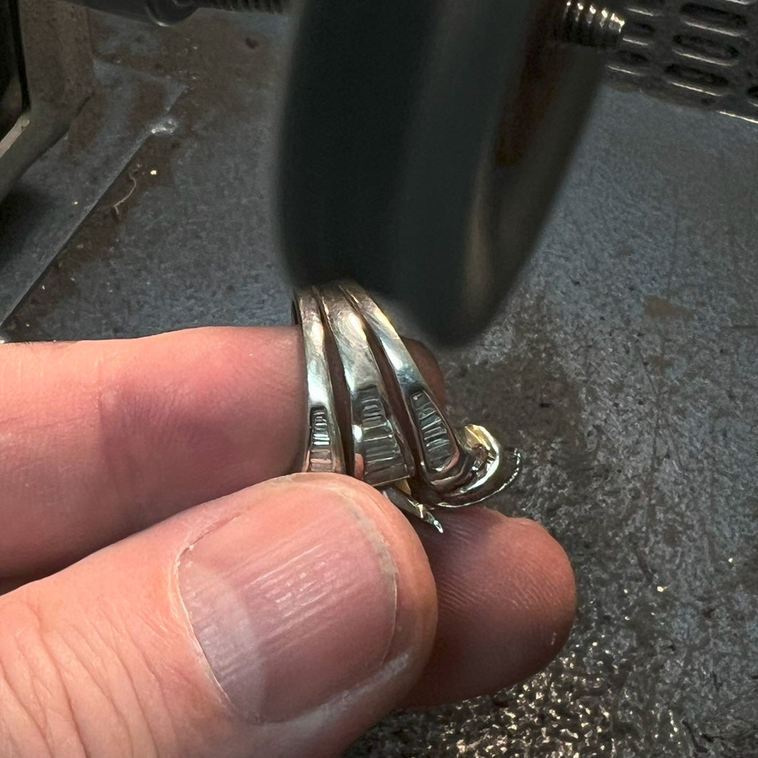 A jewelry holding a ring in their hand under a polishing machine.