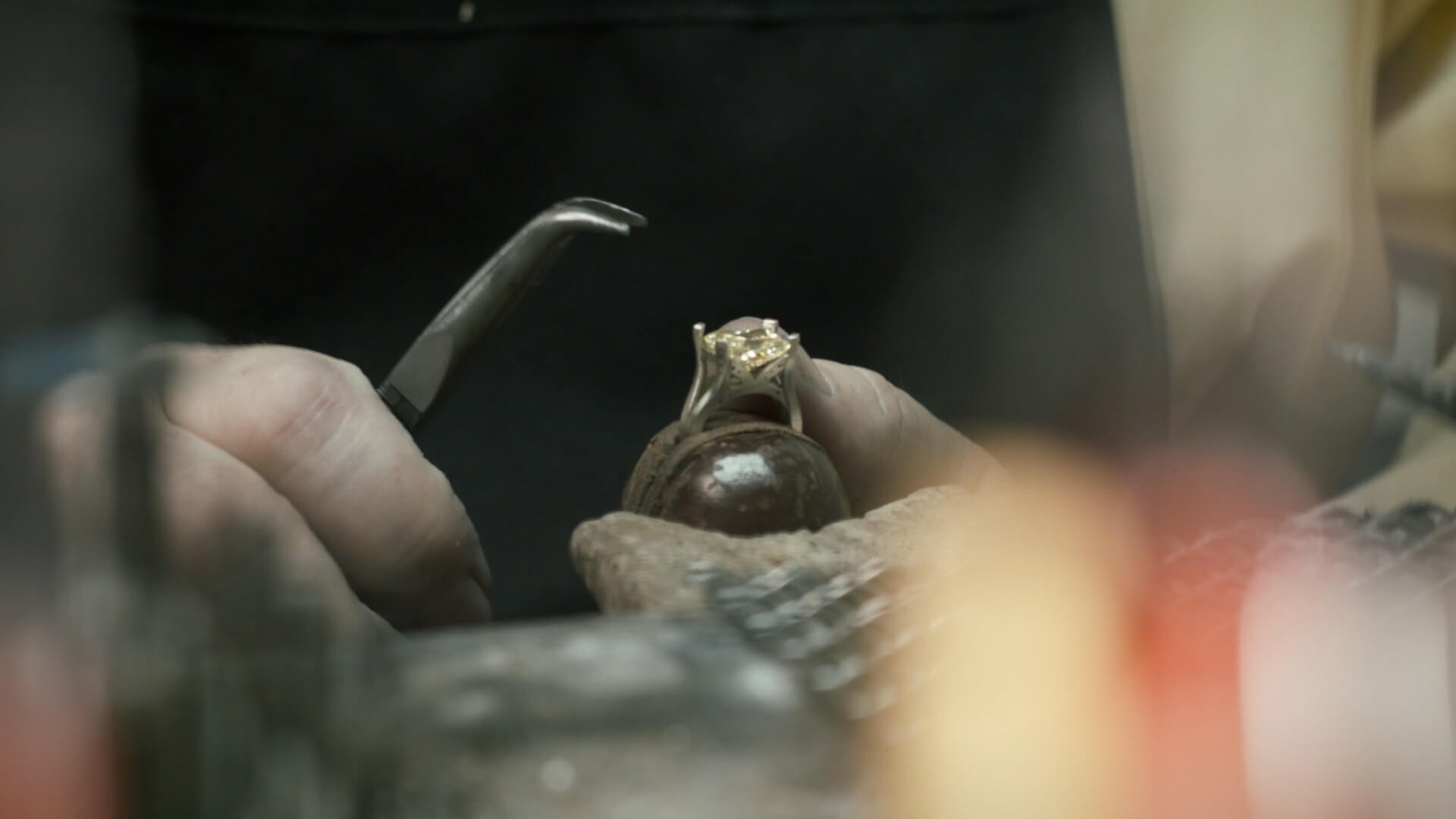 A close-up of a jewelry hand tightening a prong on a ring. The prong is loose and needs to be tightened to secure the stone in the ring.
