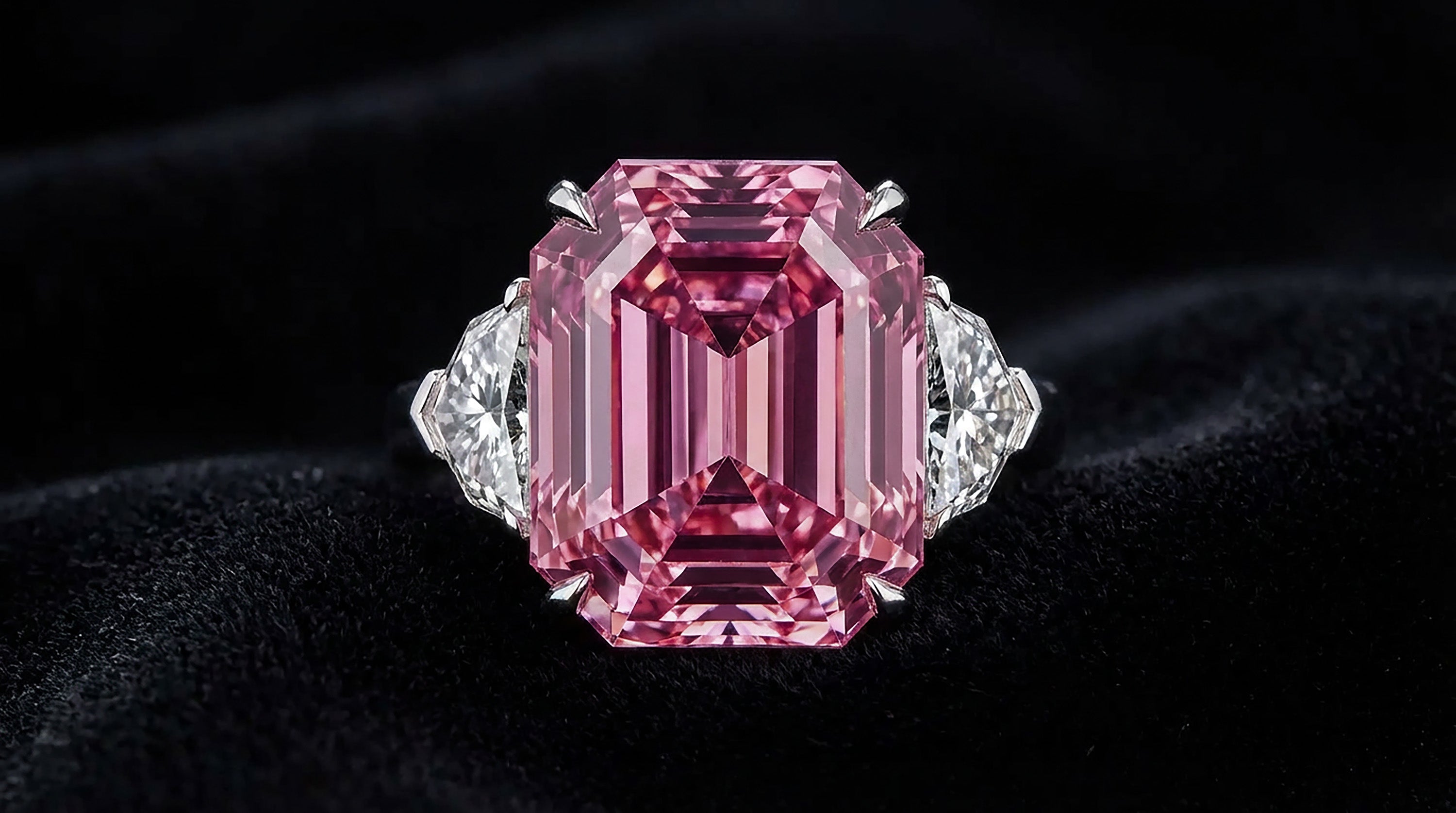 An emerald-cut pink diamond set in a white gold ring, showing the saturated color that drives value.