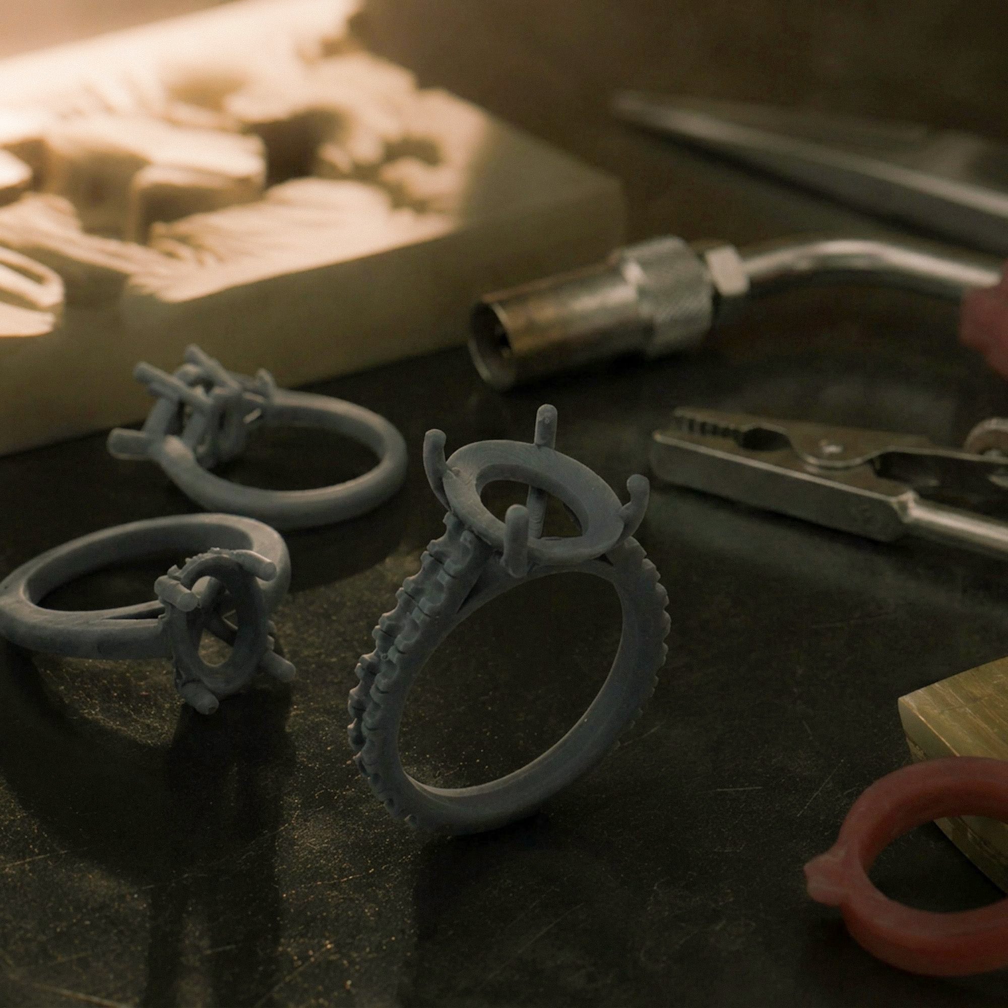 Three dark grey 3D printed engagement ring prototypes resting on a jeweler's workbench during the custom design process.