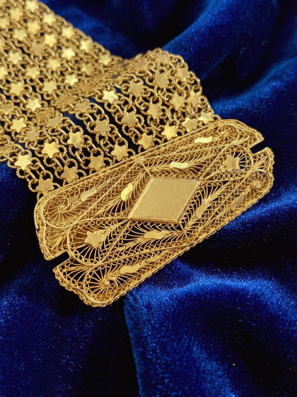 High-karat 22k gold estate bracelet with wide star mesh design. Features a substantial filigree box clasp with scroll details. Vintage yellow gold jewelry on a blue velvet background.